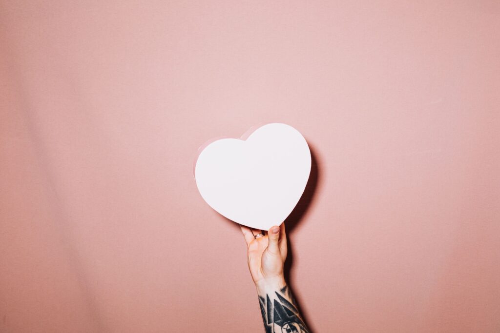 Hand holding a white heart on rose background